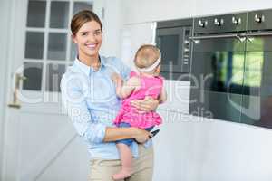Woman carrying baby girl in kitchen