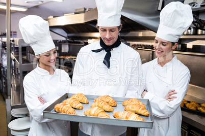 Three chefs holding a tray of baked croissant