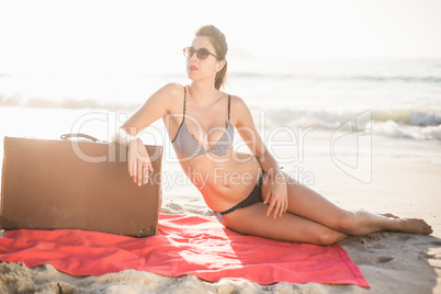 Glamorous woman in bikini sitting next to suitcase on the beach