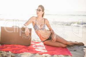 Glamorous woman in bikini sitting next to suitcase on the beach