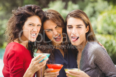 Female friends making face while drinking cocktail