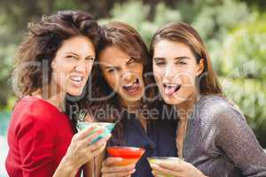 Female friends making face while drinking cocktail
