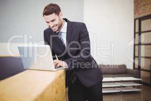 Businessman using laptop while leaning on counter