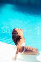 Happy woman in bikini sitting by pool side