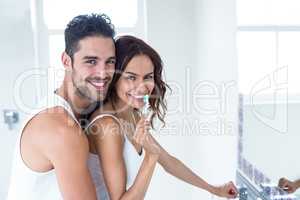 Woman brushing teeth while husband embracing her