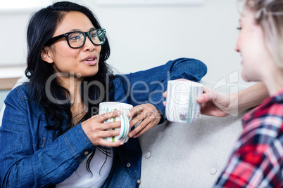 Young woman talking with female friend while drinking coffee