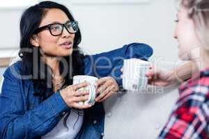 Young woman talking with female friend while drinking coffee