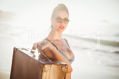 Glamorous woman in bikini holding an old suitcase