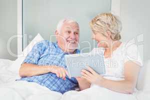 Cheerful senior couple using digital table on bed