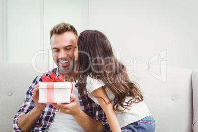 Father holding gift box while daughter kissing