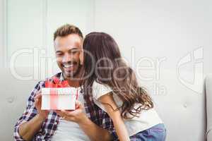 Father holding gift box while daughter kissing