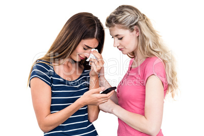 Sad young woman crying while holding mobile phone with friend