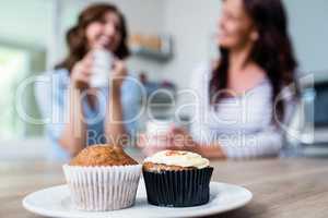Muffin and cupcake served on table with friends sitting in backg