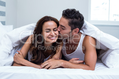 Smiling man kissing woman while lying under blanket