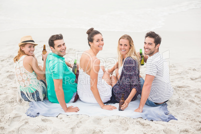 Group of friends sitting side by side on the beach with beer bot