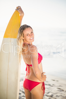 Woman in bikini standing with a surfboard on the beach