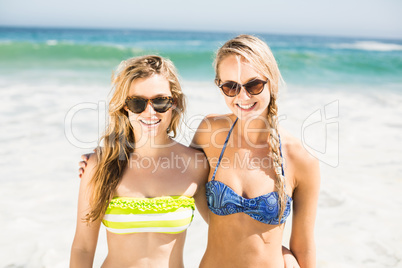 Portrait of two happy women in bikini standing on the beach