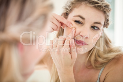 Concerned young woman looking in mirror while standing