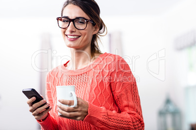 Happy young woman with mobile phone and mug