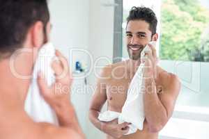 Handsome man wiping face while looking in mirror