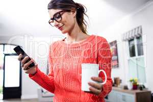 Young woman with cup using mobile phone