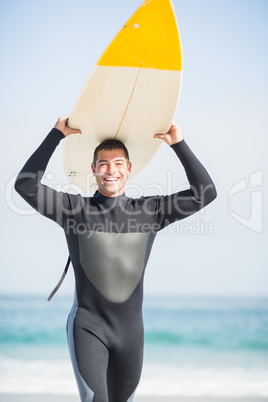 Happy man in wetsuit carrying surfboard over head