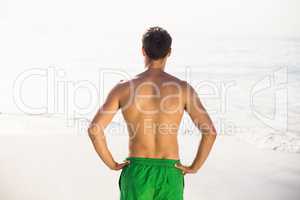 Rear view of man in swim shorts standing on beach