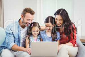 Family smiling and looking in laptop on sofa