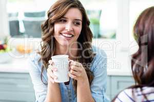 Smiling friends holding coffee mugs while sitting at table