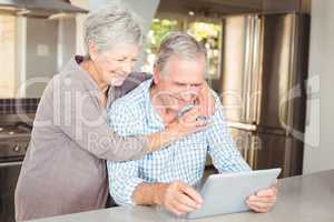 Happy senior woman embracing man using tablet
