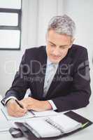 Businessman writing in spiral notebook in office
