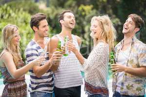 Group of friends toasting beer bottles near pool