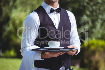 Handsome waiter holding a tray with cup of coffee