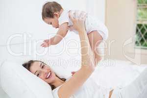 Happy mother playing with baby on bed