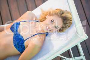 Portrait of woman in blue bikini lying on sun lounger by poolsid