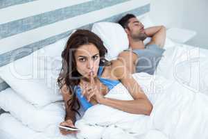 Portrait of woman with finger on lips besides husband sleeping o
