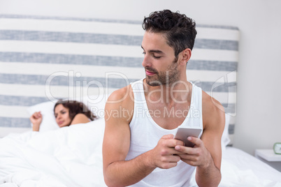 Man using mobile phone while wife sleeping on bed