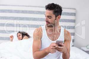 Man using mobile phone while wife sleeping on bed