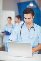 Male doctor working on laptop with colleagues discussing