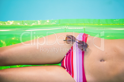Mid section of a woman in bikini lying on air bed with sunglasse