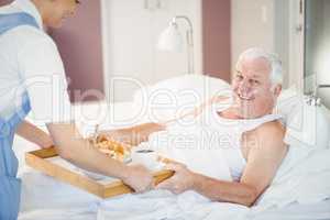 Nurse offering breakfast to senior man lying on bed