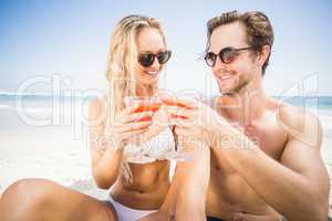 Young couple in sunglasses toasting cocktail glass on the beach