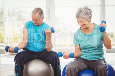 Smiling senior couple holding dumbbells while exercising