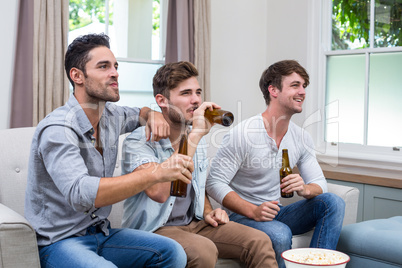 Young male friends drinking beer while watching TV