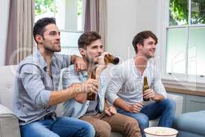 Young male friends drinking beer while watching TV