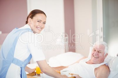 Portrait of nurse offering breakfast to senior man lying on bed