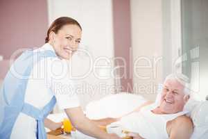 Portrait of nurse offering breakfast to senior man lying on bed