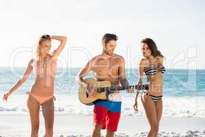 Happy friends dancing and playing guitar on the beach
