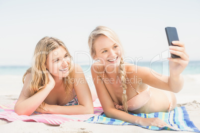 Two friends taking selfie while lying on the beach