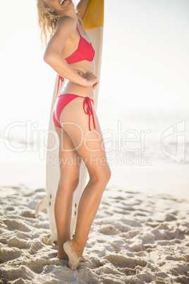 Woman in bikini standing with a surfboard on the beach